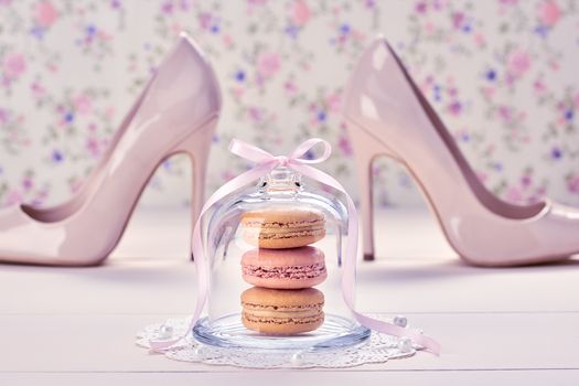 Woman essentials fashion accessories. Macarons french dessert, luxury beige shoes high heels, pearl, ribbon. Creative wedding set, vanilla wood, floral background. Romantic, still life. Retro vintage 