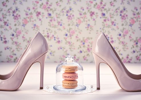 Woman essentials fashion accessories. Macarons french dessert, luxury beige shoes high heels, pearl, ribbon. Creative wedding set, vanilla wood, floral background. Romantic, still life. Retro vintage 