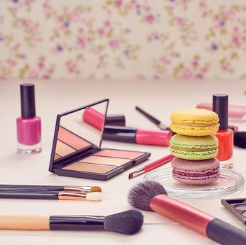 Still life, fashion woman essentials cosmetics. Beauty makeup accessories. Macarons french dessert. Lipstick, brushes, eyeshadow, false eyelashes, mascara.Unusual creative set. Vanilla wood background