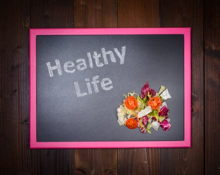 In the picture a blackboard, on the left side with written "Healthy Life" and on the right side salad of vegetables on wooden background