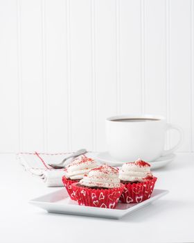 Three red velvet cupcakes on a plate served with coffee.