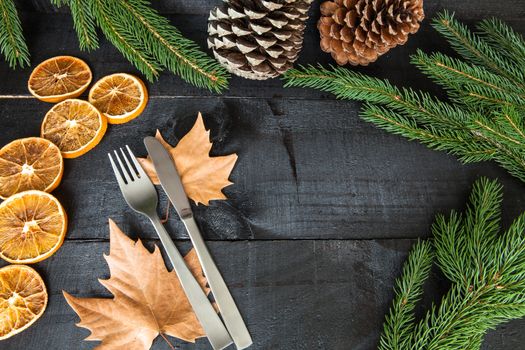 Composition of cutlery on wood background for branches and a decorative dry oranges, pain fruit and leafs for informal dinners or family celebrations in autumn winter season