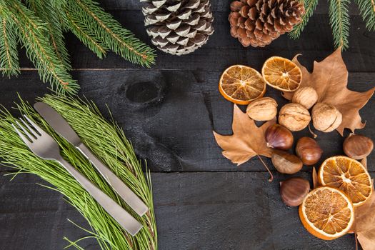 Composition of cutlery on wood background for branches and a decorative dry oranges, pain fruit and leafs for informal dinners or family celebrations in autumn winter season
