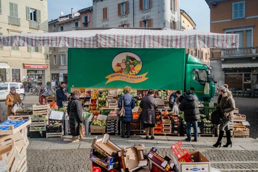 Street market, fruit and vegetables stand, people stopping to shop and passing by. Cremona, Italy  street market, January 2016