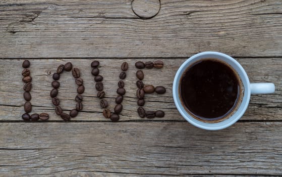 Cup of coffee on wooden background and LOVE coffee beans