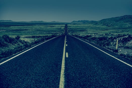 Down the Road. Straight Desert Highway in Bluish Color Grading. Straight Road to Nowhere.