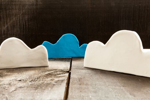 The image shows clouds of clay imitating the clouds and the concept of technological clouding over wooden background as if it were an illustration