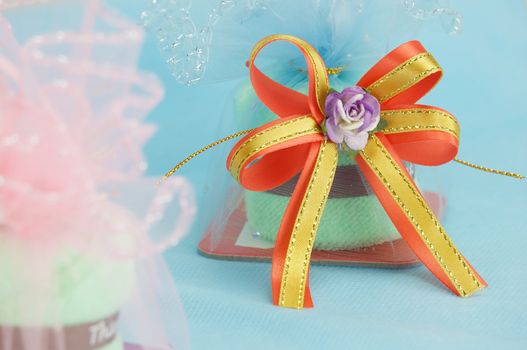 Purple flower with gold and orange ribbon bow have blur pink gift of wedding as foreground and soft blue bag as background.