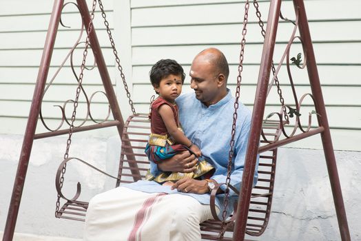 Indian parent and child sitting on a swing. Traditional India family outdoor portrait.