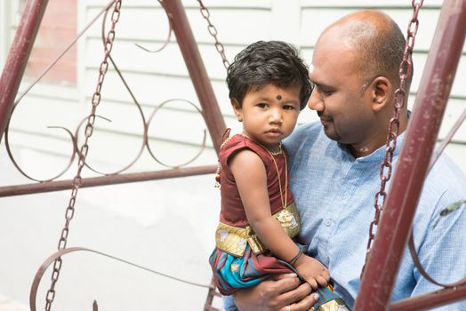 Traditional India family outdoor portrait. Indian parent and child sitting on a swing. 