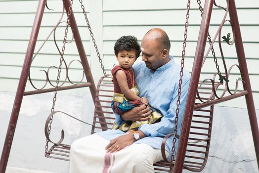Indian father and daughter sitting on a swing. Traditional India family outdoor portrait.