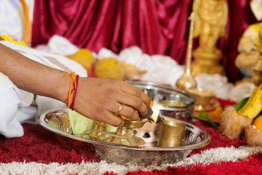 Traditional Indian Hindu religious praying items in ear piercing ceremony for children. Focus on the hand and oil lamp. India special rituals heritage.