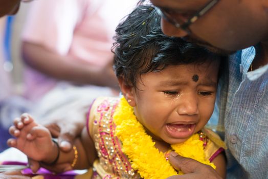 Father pampered his baby girl that crying in the karnavedha events. Traditional Indian Hindus ear piercing ceremony. India special rituals.