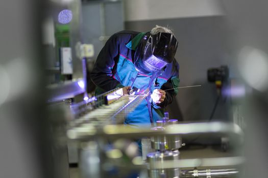 Industrial worker with protective mask welding inox elements in steel structures manufacture workshop or metal factory.