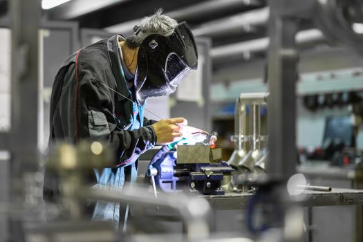 Industrial worker with protective mask welding inox elements in steel structures manufacture workshop or metal factory.