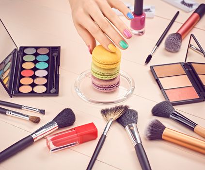 Still life, fashion woman essentials cosmetics. Beauty makeup accessories. Macarons french dessert. Lipstick, brushes, eyeshadow, mascara, hand colorful nails. Unusual creative set.Vanilla background