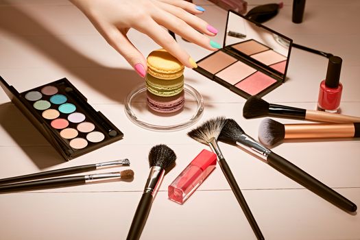 Still life, fashion woman essentials cosmetics. Beauty makeup accessories. Macarons french dessert. Lipstick, brushes, eyeshadow, mascara, hand colorful nails. Unusual creative set.Vanilla background