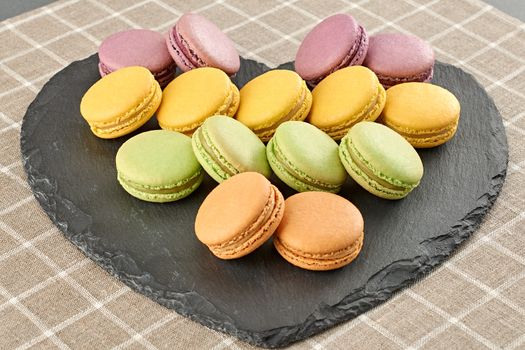 Still life, macarons sweet colorful, heart black placemat. Fresh pastel french traditional delicious dessert. Unusual creative romantic, background. Concept for love story. Valentines Day.Food closeup