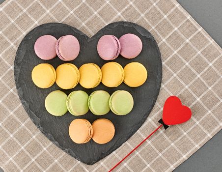 Still life, macarons sweet colorful, black placemat. Heart made of red wood. Fresh pastel french traditional dessert. Unusual creative romantic, background. Concept love story. Valentines Day.