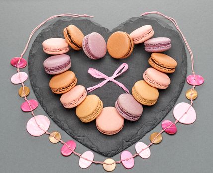 Still life, macarons sweet colorful, heart shape, black placemat. French traditional delicious dessert, necklace, bow. Unusual creative romantic, gray background. Concept for love story.Valentines Day