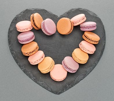 Still life, macarons sweet colorful, heart shape, black placemat. French traditional delicious dessert. Unusual creative romantic, gray background. Concept for love story.Valentines Day