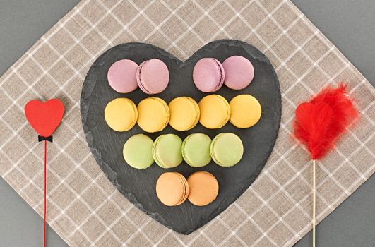 Still life, macarons sweet colorful, black placemat. Hearts couple of red wood. Fresh pastel french traditional dessert. Unusual creative romantic, background. Concept love story. Valentines Day.