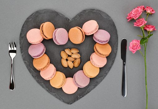 Still life, macarons sweet colorful, heart shape and fork knife. Black placemat, roses almond. French dessert, table setting. Unusual creative romantic, background. Concept love story.Valentines Day