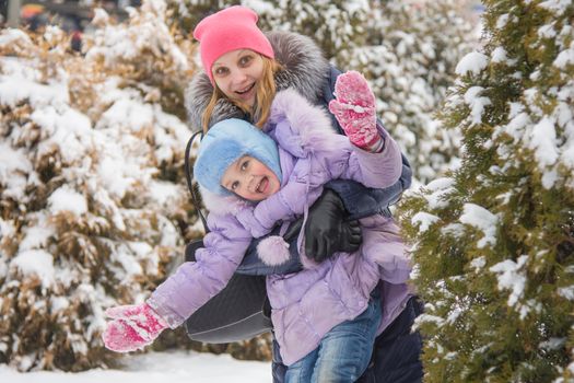 Five-year girl and young mother walking on snow-covered coniferous forest