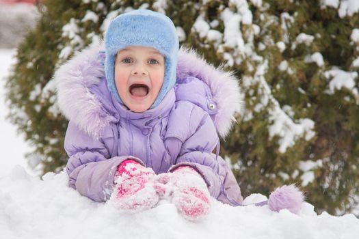 Five-year girl lies on snowdrift snow against a snowy background Trees
