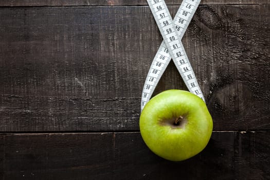 The image shows apple surrounded by a measuring tape referring to diet and health concept on wooden background