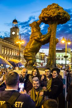 Madrid, Spain - Jan 23, 2016:  Group of friends posing by statue of a bear and a madrone tree on busy Puerta del Sol square at dusk on January 23th, 2016 in Madrid, Spain. 
