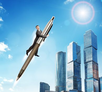 Businessman flying on big pen above city scape