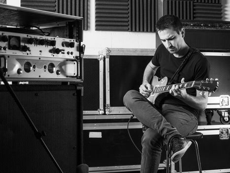 Photo of a man sitting backstage practicing his guitar.