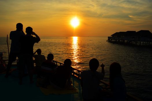 Silhouette of couple lovers and tourist watching the sun setting on cruise over sea. People relaxing at the seaside during holiday and enjoying beautiful sunset, Maldives