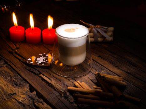 Frothy, layered cappuccino in a clear glass mug. Three red candles, cinnamon sticks and sweets. Romantic concept