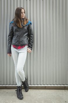 Young Teen Girl Wearing Leather Jacket Standing Against Metal Wall and Looking to the Side.