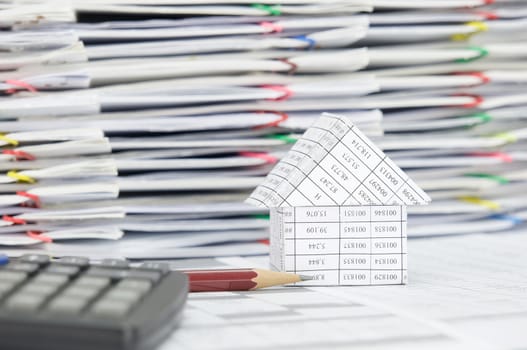 Close up brown pencil and house on finance account have blur calculator and pile of document with colorful paperclip as foreground and background.