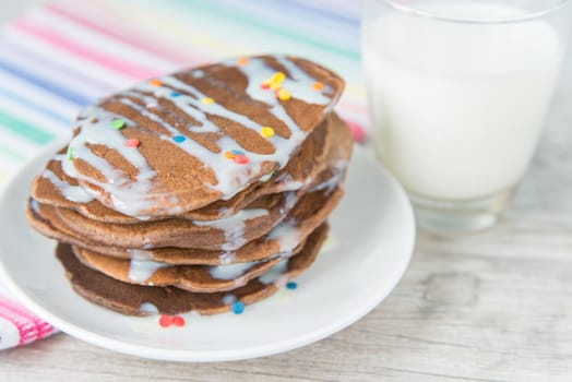 Decorated chocolate pancakes with the glass of milk on the coloured napkin