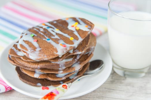 Decorated chocolate pancakes with the glass of milk on the coloured napkin