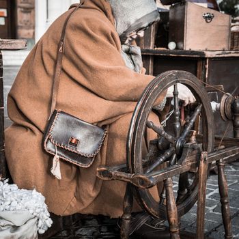 Elderly woman uses the cocoons of silkworms to spin using an old spinning wheel of wood.