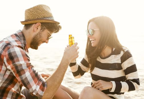 Young couple at the beach having fun, laughing and drinking beer