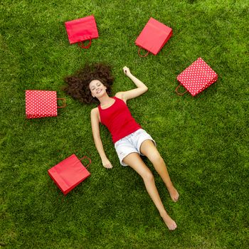 Beautiful and happy young woman lying on the grass surrounded by red gift bags