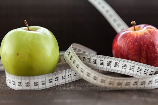 The image shows apple surrounded by a measuring tape referring to diet and health concept on wooden background