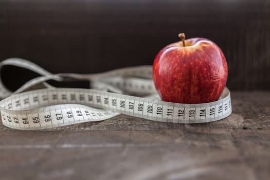 The image shows apple surrounded by a measuring tape referring to diet and health concept on wooden background