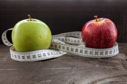 The image shows apple surrounded by a measuring tape referring to diet and health concept on wooden background