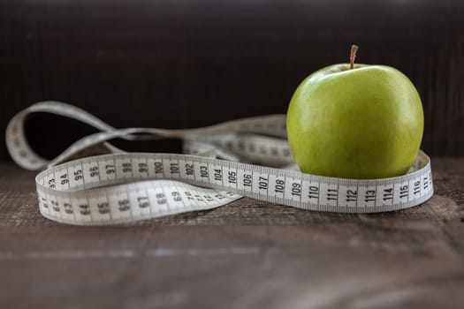 The image shows apple surrounded by a measuring tape referring to diet and health concept on wooden background