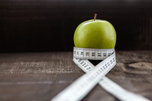 The image shows apple surrounded by a measuring tape referring to diet and health concept on wooden background