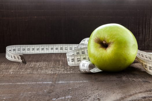 The image shows apple surrounded by a measuring tape referring to diet and health concept on wooden background