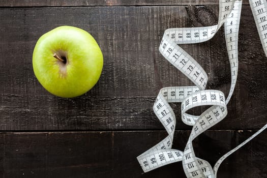 The image shows apple surrounded by a measuring tape referring to diet and health concept on wooden background