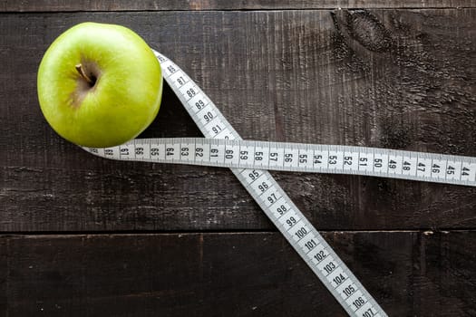 The image shows apple surrounded by a measuring tape referring to diet and health concept on wooden background